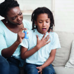 Black mother holding asthma inhaler for daughter
