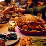 Close up of stuffed turkey during Thanksgiving meal with family toasting in the background.