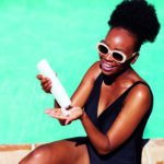 Beautiful Black woman applies sunscreen sitting by pool in summer sun